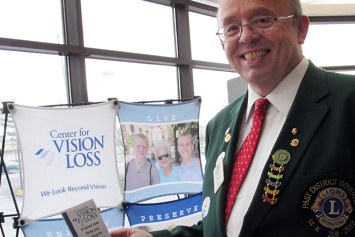 A photo of a Lions Club member in front of agency signage