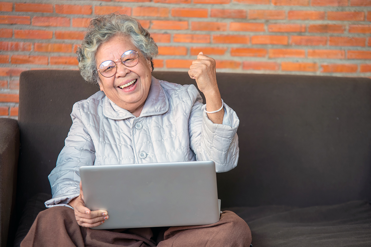 An older woman with glasses using a laptop computer on her living room sofa
