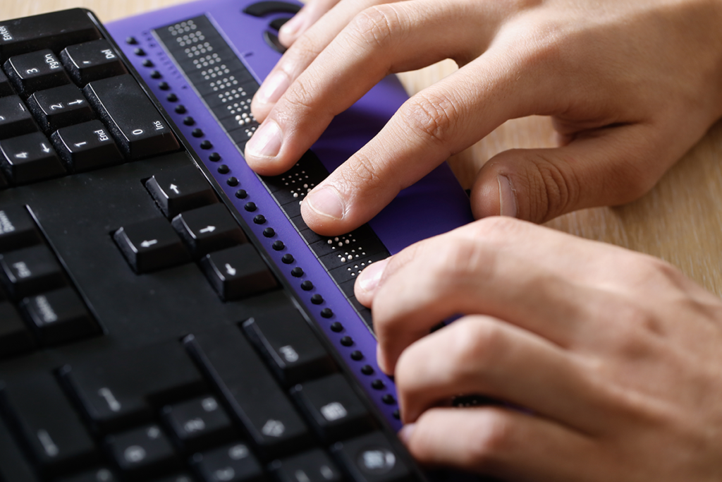 Photo of a person's hands on a Braille bar connected with a computer keyboard
