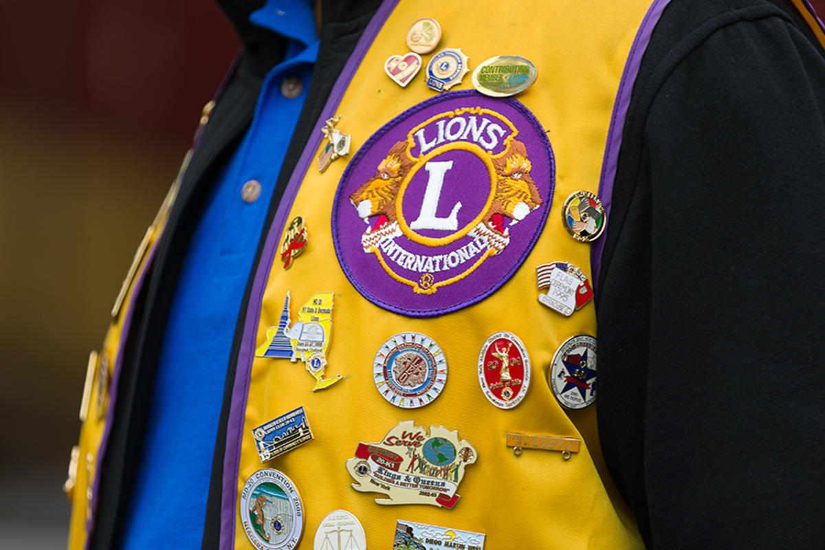 A person wearing a blue shirt and a yellow vest with the Lions International emblem and several Lions pins