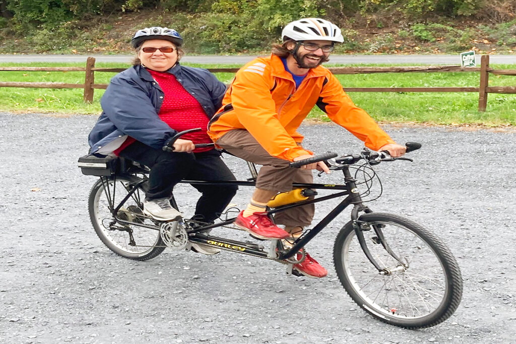 Image: Photo of a female Sights for Hope smiling as she rides on the back of a tandem bicycle.