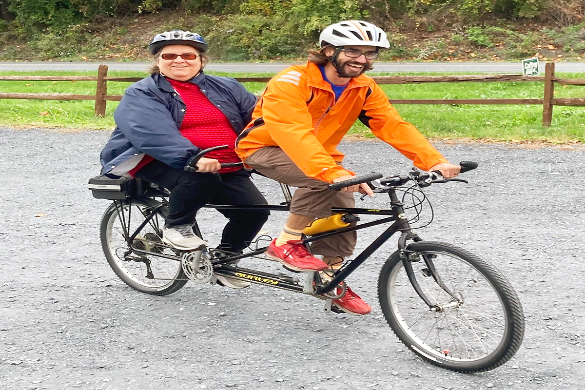 A female Sights for Hope smiling as she rides on the back of a tandem bicycle