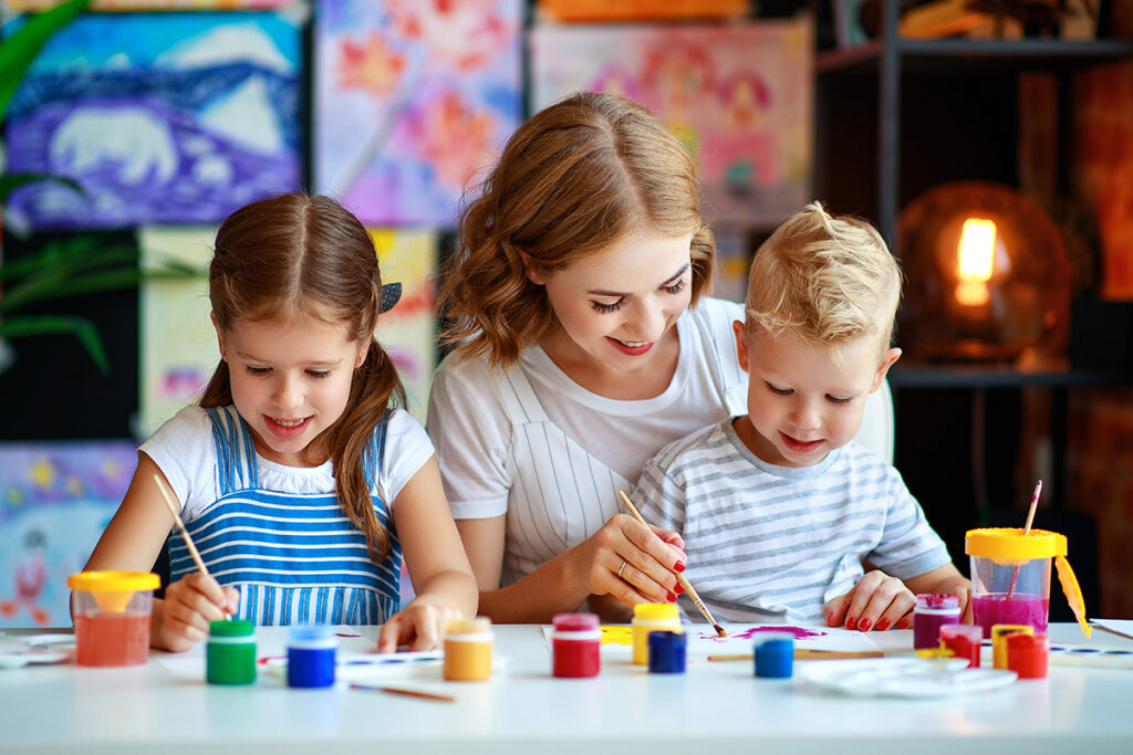 Photo of a mother and her two young children painting and drawing together