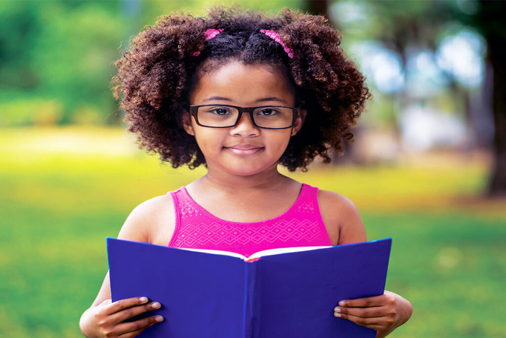 Photo of an African-American girl wearing glasses and reading a book outside; photo from Pennsylvania Vision Foundation