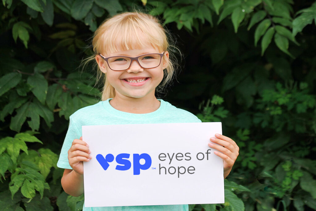 Photo of a happy young girl holding a sign with the VSP Eyes of Hope logo