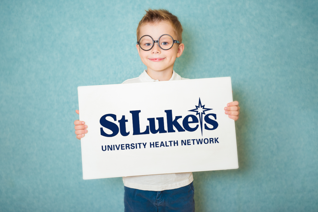 Photo of a young boy with glasses holding a sign with the St. Luke's University Health Network logo