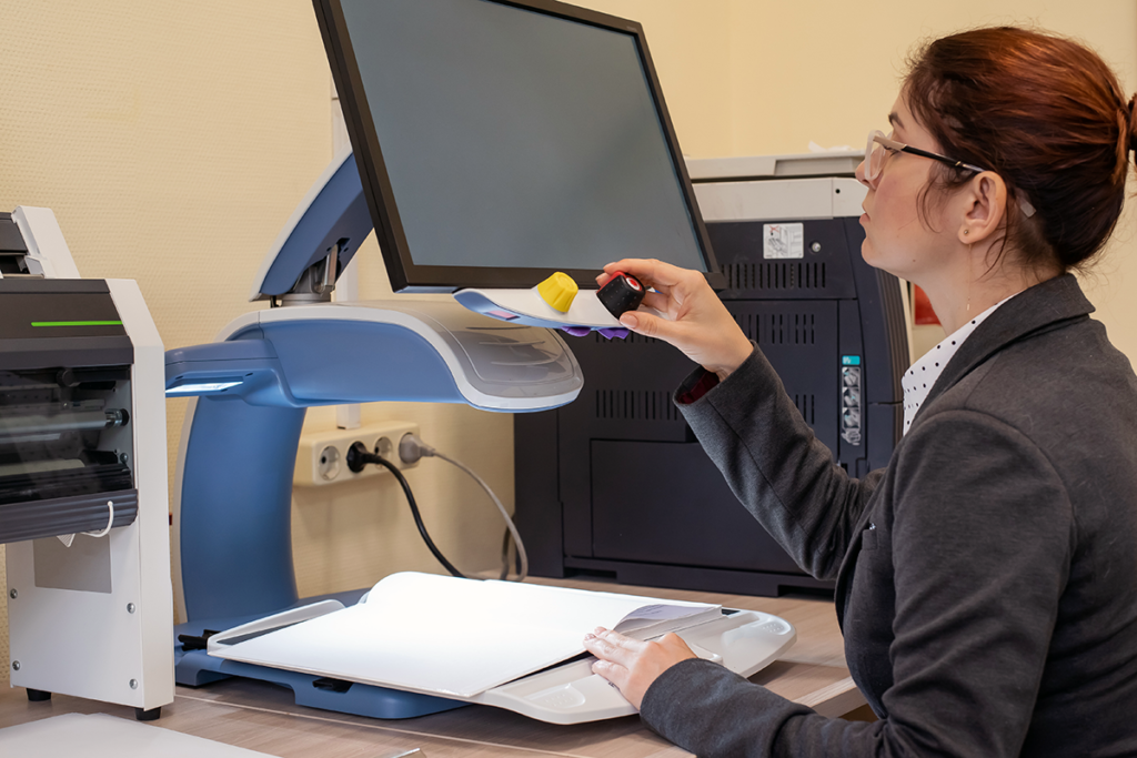 Photo of a young female in an office using an enlarger to read a document
