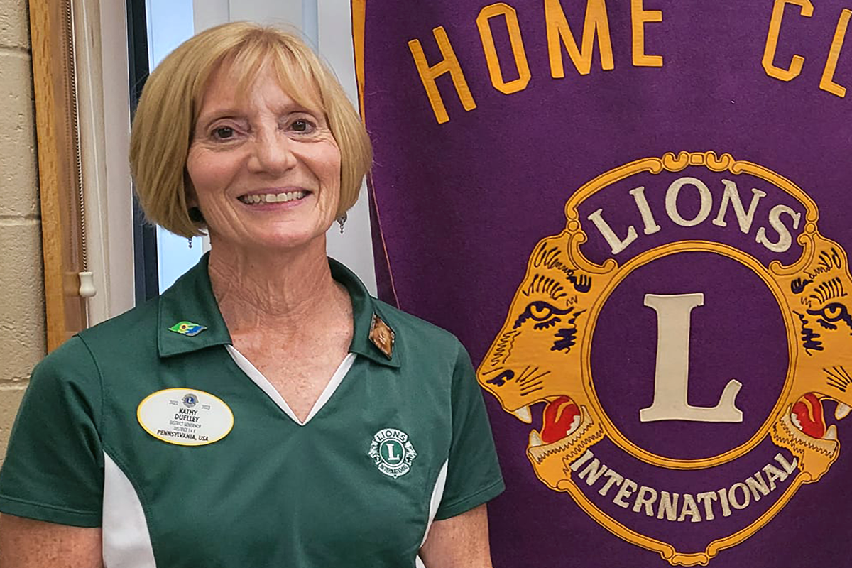Kathy Duelley in front of a Lions Club banner