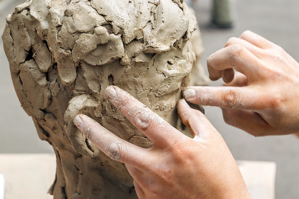 Photo of two hands working on a clay sculpture