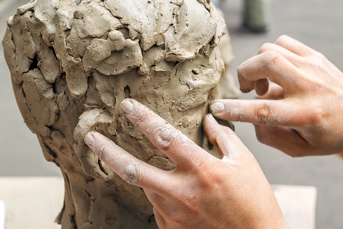 Two hands working on a clay sculpture