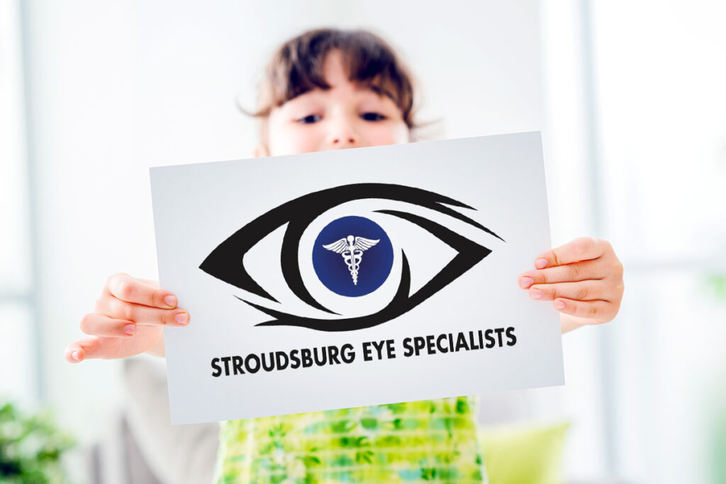 Photo of a young girl in a green dress holding up a white sign with the Stroudsburg Eye Specialists logo
