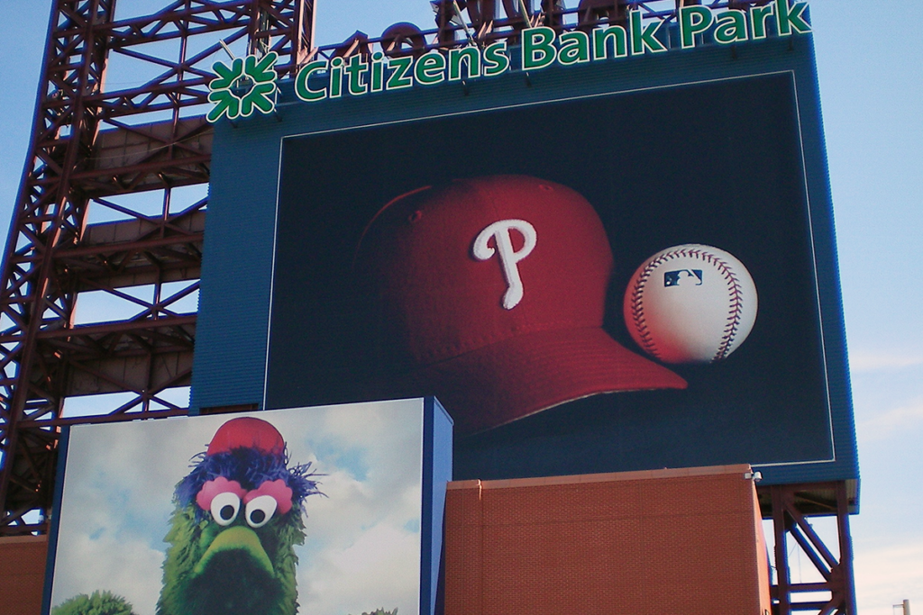 Citizens Bank Park, home of the Philadelphia Phillies. Shown on the exterior structure are a sign with the name Citizens Bank Park, pictures of a Phillies baseball cap and a baseball, and a photo of the Phillie Phanatic mascot.