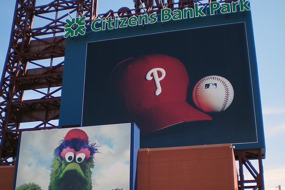 Photo of Citizens Bank Park, home of the Philadelphia Phillies. Shown on the exterior structure are a sign with the name Citizens Bank Park, pictures of a Phillies baseball cap and a baseball, and a photo of the Phillie Phanatic mascot.