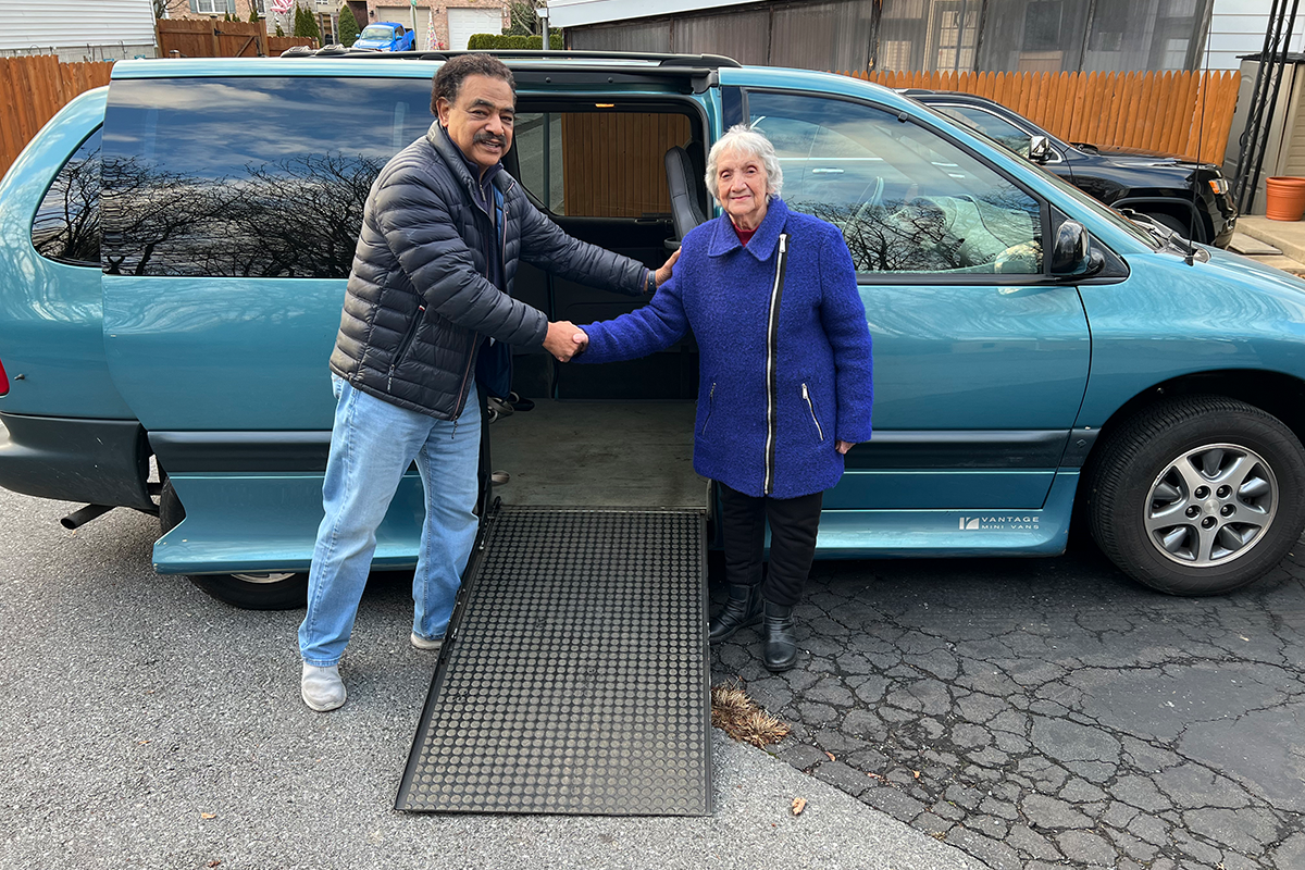 Sights for Hope Transport Driver Byron Jackson and Elaine Bartholomew shaking hands in front of a specially equipped blue van that Elaine has donated