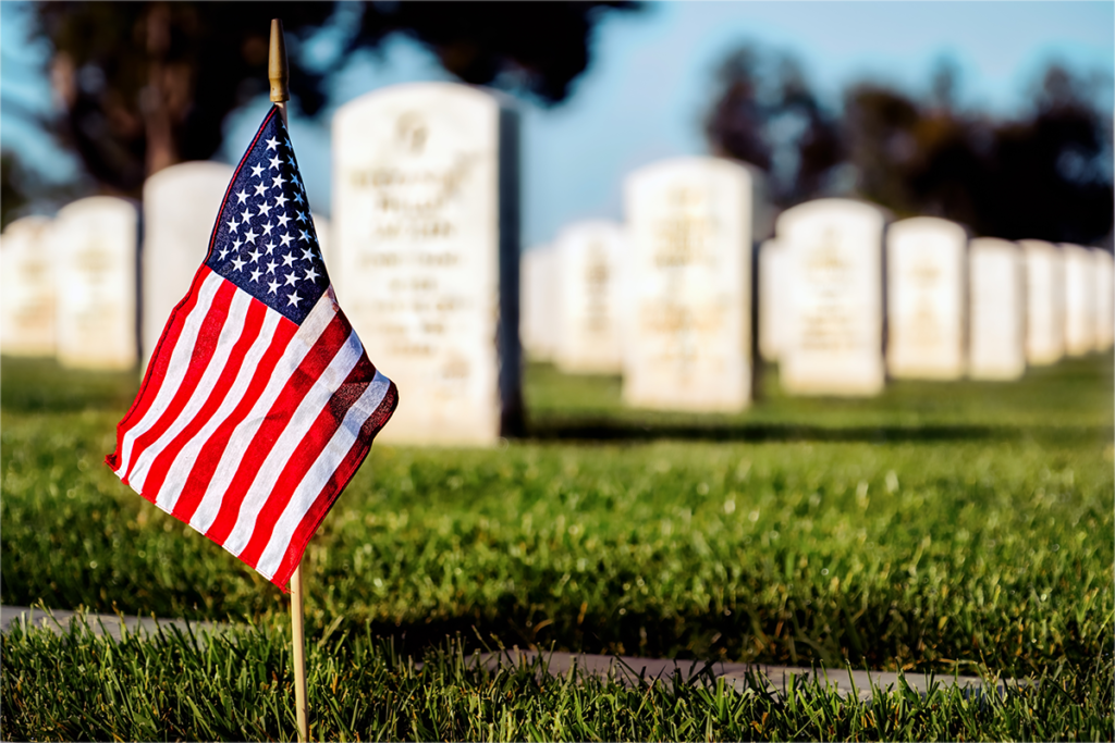 A single American flag planted in the grass near several graves in a cemetery