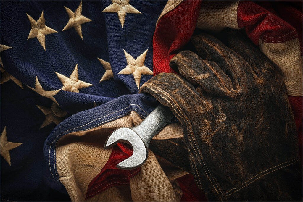 An American flag and a worn work glove holding a wrench