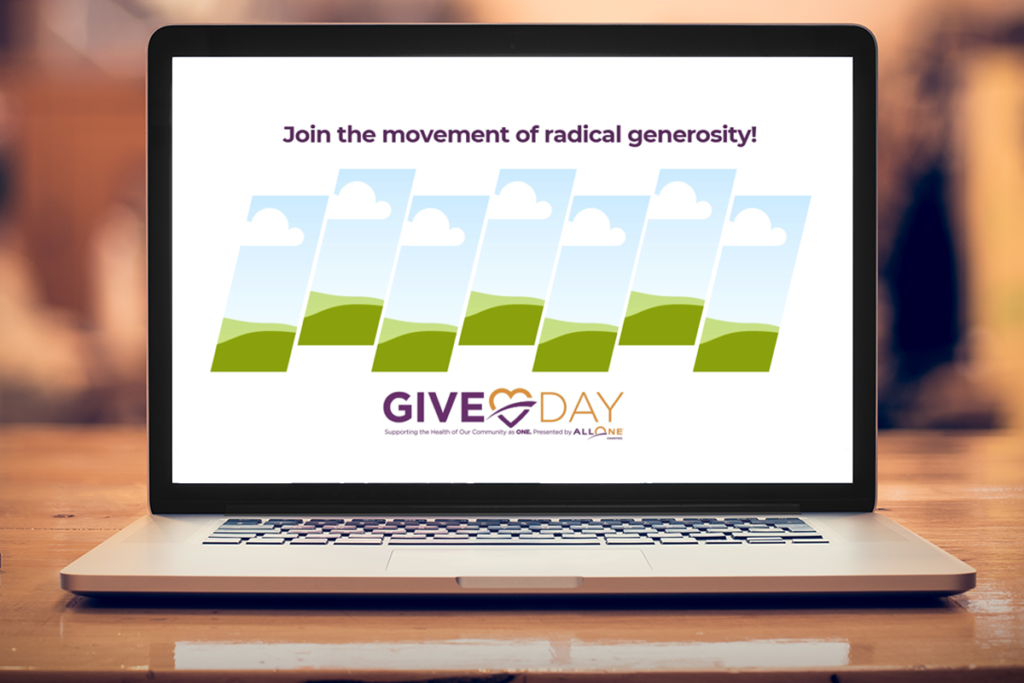 A laptop computer on a wooden table with the Give Day logo on the screen and the words "Join the movement of radical generosity!"