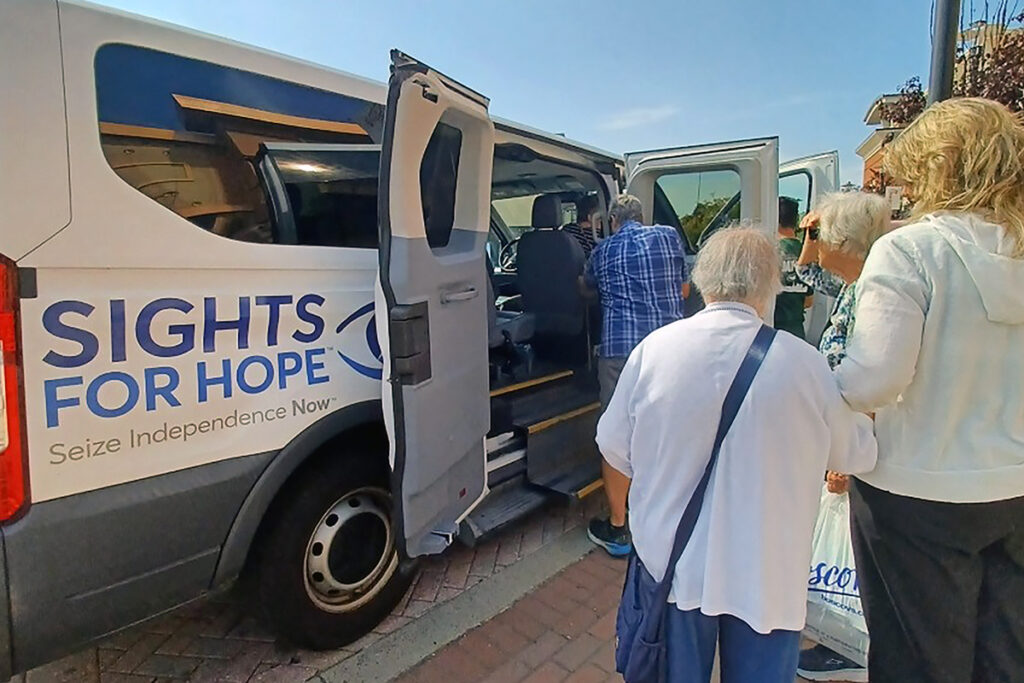 A group of individuals board a van labeled with the Sights for Hope logo, promoting independence. The atmosphere is supportive and community-focused.