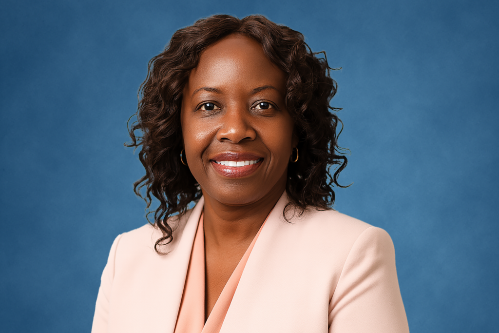 A woman with curly hair smiles confidently in a light pink blazer against a blue background. The tone is professional and approachable.