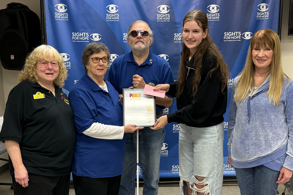 Five people stand smiling in front of a "Sights for Hope" banner. One person holds a certificate, conveying an atmosphere of achievement and celebration.