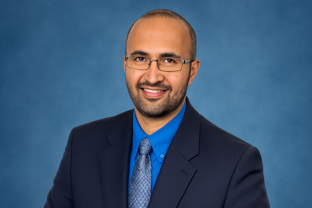 Vinod Namboodiri, Ph.D., in a dark suit, navy blue shirt, and blue tie