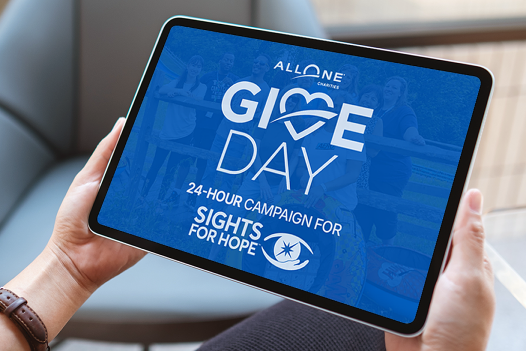 A woman holds a table computer displaying a graphic with the All One Charities Give Day logo, the words "24-hour campaign for," and the Sights for Hope logo