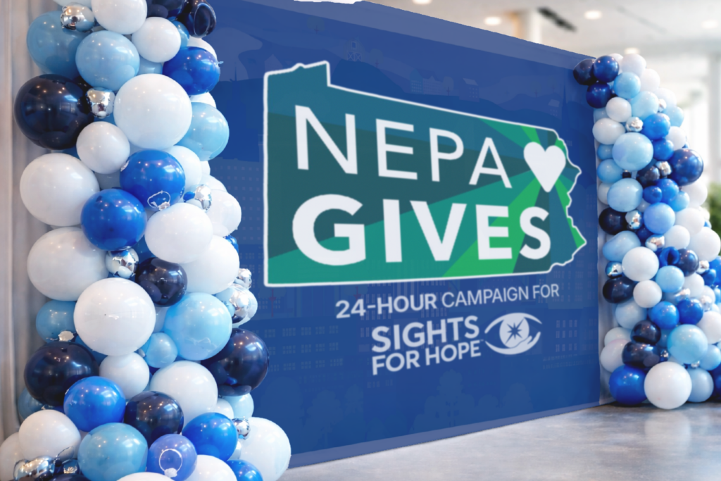 Balloon columns in blue, white, and silver surrounds a sign reading "NEPA Gives 24-hour campaign for Sights for Hope" in a modern indoor setting.