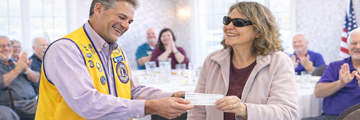 A Lions Club member presents a check to a woman living with vision loss at a community gathering.