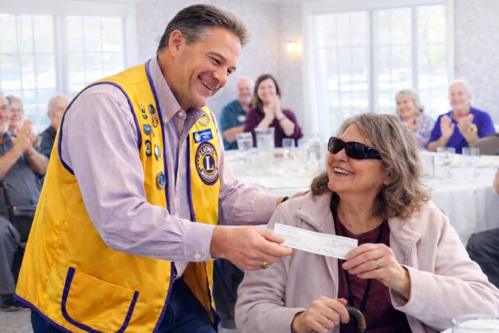 A Lions Club member presents a check to a woman living with vision loss at a community gathering.