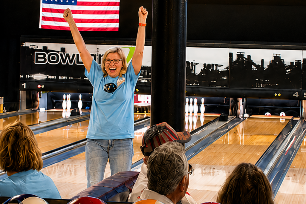 A bowler celebrates with both arms raised after a successful roll during the 2026 Marian Boehm Memorial Bowlers for Sight Tournament as fellow participants watch from nearby lanes.