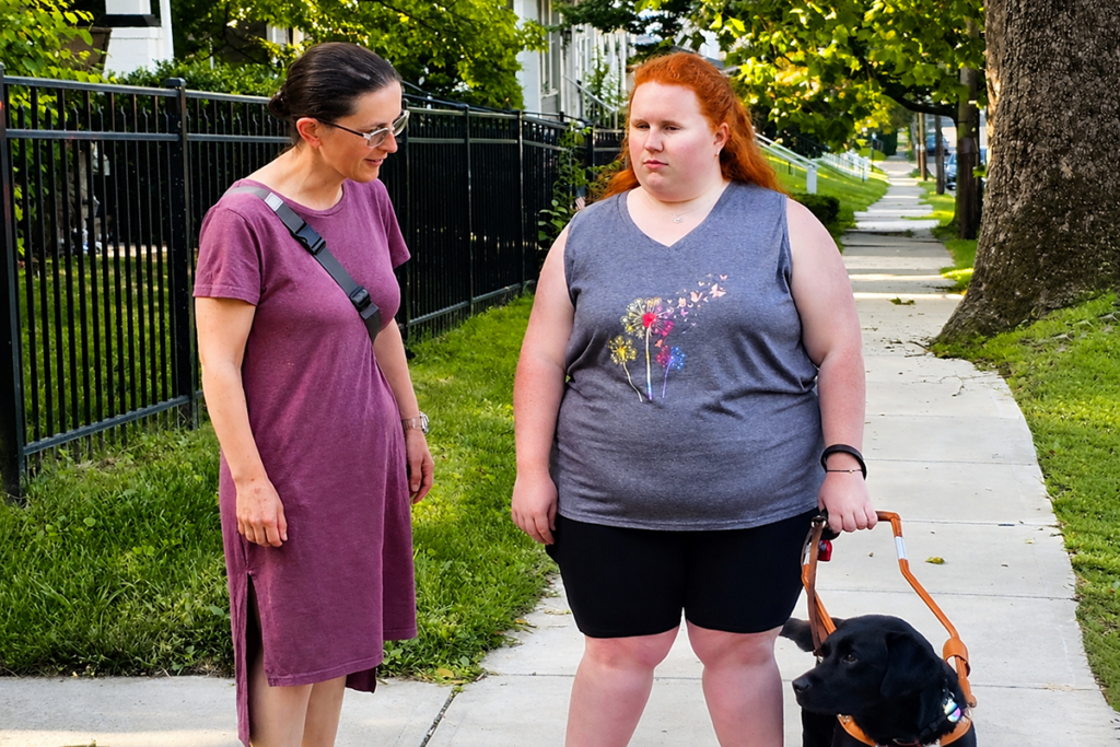 Sights for Hope contract Orientation & Mobility Instructor Nadya Krause works with a client and her black guide dog during an outdoor travel lesson on a residential sidewalk.