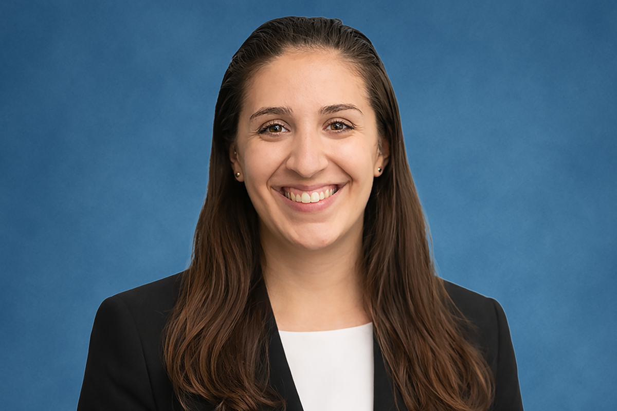 Promotional image of Erica Vibert, a smiling woman with long brown hair, wearing a black blazer over a white top, against a textured blue background.