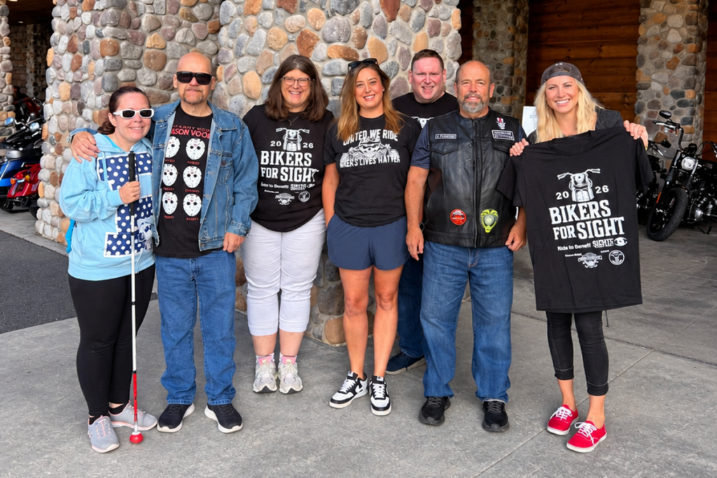 Bikers for Sight riders and Sights for Hope team members pose with event sponsors, one of whom is holding up a black event shirt.