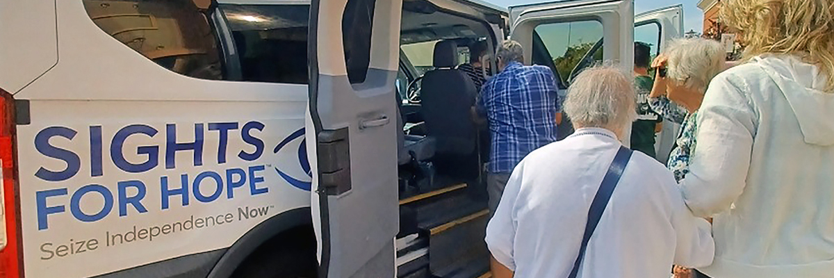 A group of individuals boarding a white van labeled with the Sights for Hope logo.