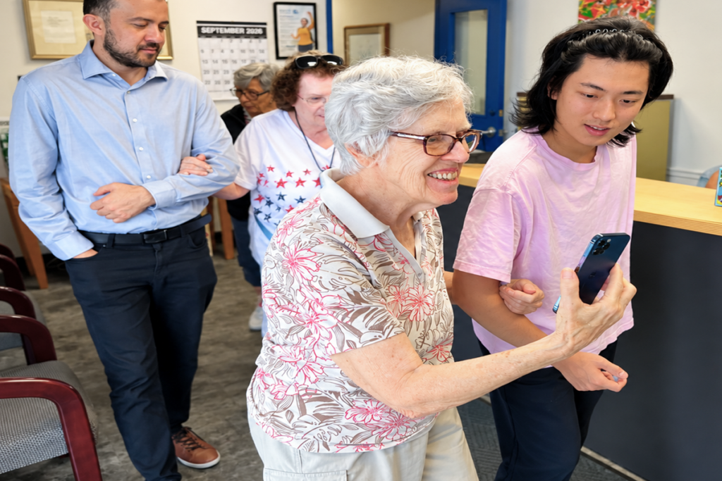A Sights for Hope client smiling while testing the MABLE Maps indoor navigation app on a smartphone with assistance from a Lehigh University graduate student. Other clients and students also are testing the technology in the background at Sights for Hope’s Lehigh Valley Services Center.